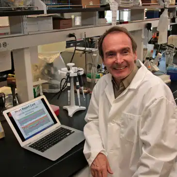 A man in lab coat sitting at a desk with laptop.