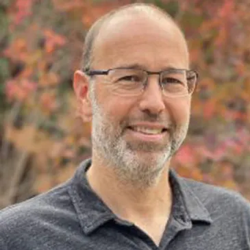 A man with glasses and a beard is smiling.