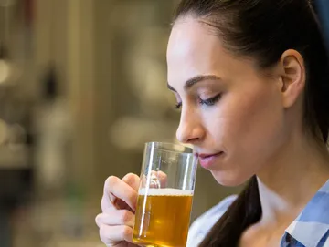 A woman drinking from a glass of beer.