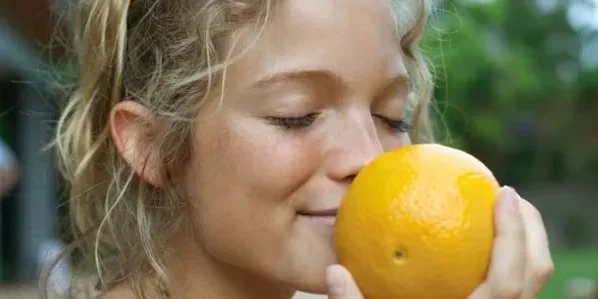 A woman is holding an orange up to her face.